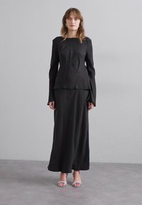 Un top negru cu mâneci lungi, cu un corset ajustat și mâneci evazate, asortat cu o fustă lungă corespunzătoare. Material neted și design minimalist.