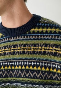 Kootud villane kampsun ümmarguse kaelusega, millel on mitmevärviline geomeetriline muster rohelises, tumesinis ja kollases ning valges. Tekstuuritud viimistlus.