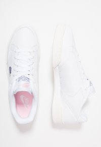 Zapatillas de cuero blanco con un acabado liso, parte superior perforada para transpirabilidad, suela plana de goma blanca y sutiles acentos en rosa por dentro.