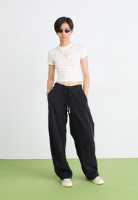 Black sweatpants with a drawstring and side pockets, paired with a fitted white t-shirt and sunglasses. Smooth, casual, and relaxed fit.