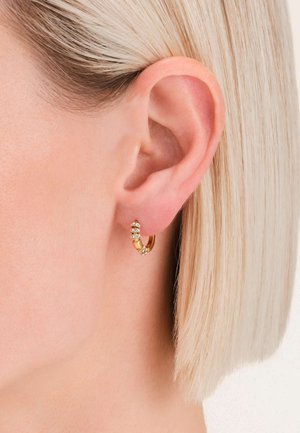 Gouden ringoorbel met drie kleine, transparante edelstenen. Strak ontwerp met een gepolijste afwerking, zichtbaar op een lichtblond kort kapsel.