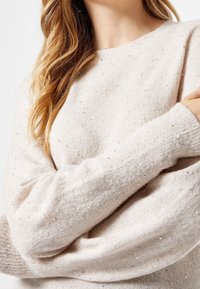 Lichtbeige gebreide trui met subtiele, verspreide pailletten, ronde halslijn en oversized mouwen met ribgebreide manchetten. Zacht, textuur materiaal.