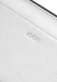 Superficie de cuero blanco texturizado con sutil logo "JOOP!" en relieve y costuras visibles a lo largo del borde.