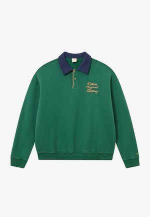 Zelena dukserica s mornarsko plavim ovratnikom, zlatnim vezom i rebrastim manžetama. Ima dizajn na preklop i mekan, teksturiran materijal. Klasik sportski stil.