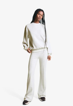 Helles graues Sweat-Outfit bestehend aus einem Langarmoberteil und weit geschnittenen Hosen mit subtilen Steppdetails. Das Material wirkt weich und gemütlich.