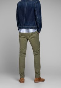 Pantaloni chino color kaki a vestibilità slim, tessuto texturizzato, abbinati a una giacca in denim scuro e scarpe in camoscio color cuoio. Presentano una camicia a righe sotto.