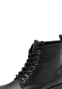 Must musta saapad paksude ümarate nööpidega, metallist silmadega ja külglibisemisega, omavad kergelt nähtavat brändi silti välisküljel.