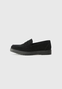 Zwarte suède instappers met een moccasin ontwerp, rubberen zool en decoratieve strik op de wreef. Glad oppervlak en ronde neus.