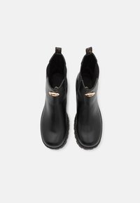 Botas de tobillo de cuero negro con un acabado suave, paneles laterales elásticos y un acento de metal en tono dorado en el costado. Suelas de goma para mayor tracción.