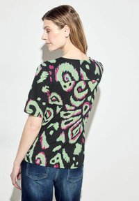 Černé tričko s krátkým rukávem, zdobené zeleným a růžovým abstraktním vzorem paisley. Měkká tkanina s volným střihem a kulatým výstřihem.