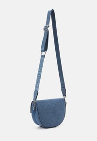 Blå denim crossbody-väska med en halvmåneform, silverdetaljer och en texturerad yta. Utrustad med en justerbar rem med varumärkeslogotyp.