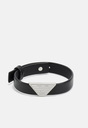 Schwarzes Lederarmband mit einem dreieckigen silbernen Metallelement, das ein gestreiftes Logodesign aufweist und einen Druckknopfverschluss hat. Glatte Textur.