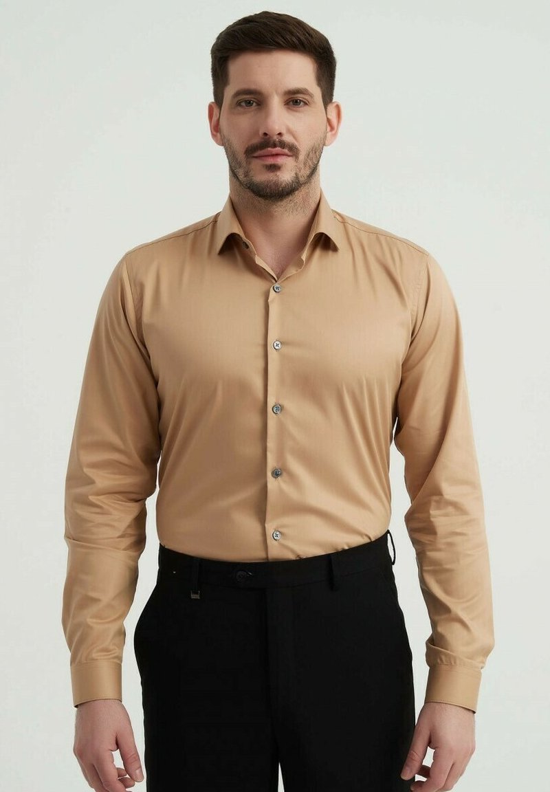 Chemise beige à manches longues avec une coupe slim, dotée d'un col pointu et de boutons en argent, assortie à un pantalon noir. Texture de tissu lisse.