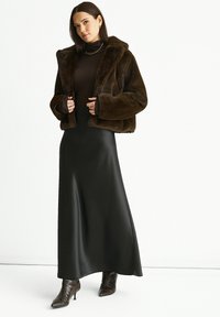 Brown faux fur cropped jacket, dark turtleneck, and long black satin skirt. Accented with fitted sleeves and pointed toe heeled boots.