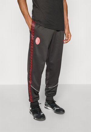 Dunkelgraue Jogginghosen mit einem roten gemusterten Seitenstreifen und weißen Paspeln, versehen mit einem Emblem auf dem linken Oberschenkel. Das Material ist aus glattem, sportlichem Stoff.