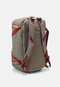 Duffle backpack in olive green fabric with light blue accents. Features adjustable red straps and a side zip pocket for storage.