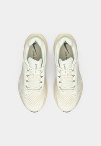 Λευκά αθλητικά παπούτσια με διάτρητο επάνω μέρος, επίπεδα κορδόνια και ανοιχτόχρωμη σόλα. Διαθέτουν μαύρο λογότυπο Nike και το κείμενο "Just Do It".