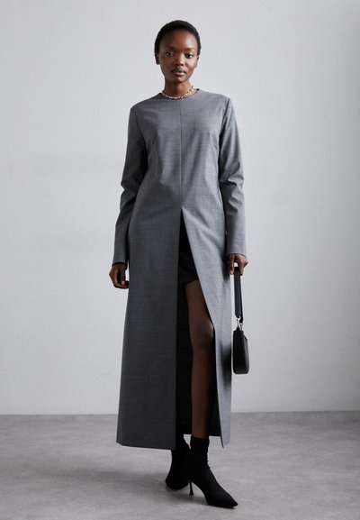 Vestido gris de manga larga con una abertura en la parte delantera, hecho de un tejido suave; combinado con botas negras hasta el tobillo y un pequeño bolso negro.