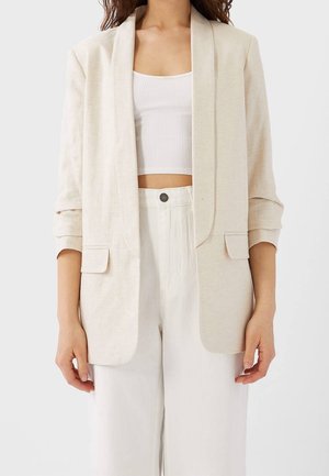 Blazer en lin beige avec un devant ouvert, des revers à crans et deux poches avant. Il présente des manches retroussées et une coupe décontractée.