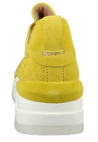 Żółte zamszowe sneakersy z grubą białą podeszwą, charakteryzujące się zaokrąglonym tyłem, minimalistycznym przeszyciem i małą pętelką z tyłu.
