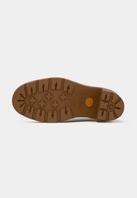 Suola in gomma marrone con tacche profonde e logo Timberland stampato vicino al tallone su uno sfondo bianco.