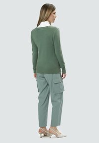 Maglione verde lavorato a maglia con orlo e polsini a coste, abbinato a pantaloni cargo azzurri chiari con tasche laterali e scarpe con tacco beige.