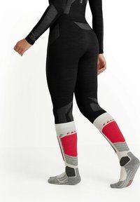 Leggings noirs avec des motifs géométriques gris, associés à des chaussettes mi-mollet comportant des accents rouges, gris et blancs, conçues pour le sportswear.