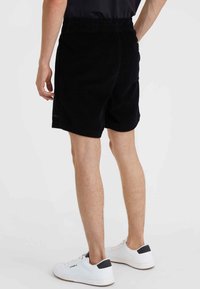 Black corduroy shorts with an elastic waistband, side pockets, and a back pocket, shown from behind, paired with white sneakers.