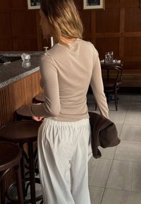 Beige pitkähihaine paita ja valkoiset väljät housut. Paidassa on pyöreä kaula-aukko, kun taas housuissa on joustava vyötärö.