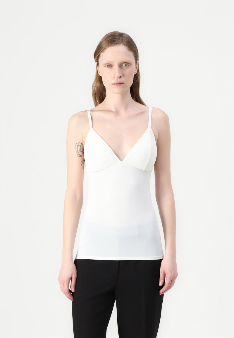 White sleeveless top with a v-neck design, soft texture, and fitted silhouette, paired with black pants. Minimalist style and clean lines.