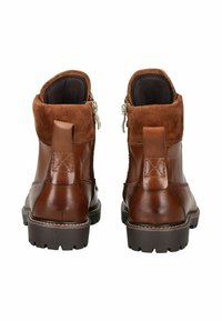 Botas tobilleras de cuero marrón y gamuza con cremalleras laterales, suelas gruesas tipo lug y tiradores, vistas desde atrás sobre un fondo blanco.