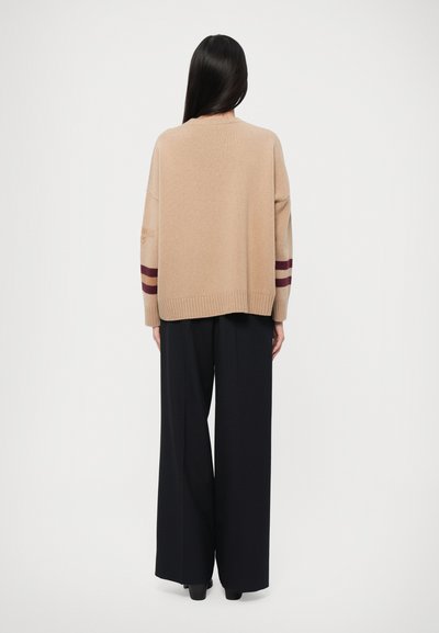 Beige strikkegenser med burgunder striper på ermene, oversized passform, ribbestrikket kant, kombinert med svarte vide bukser og hælsko.