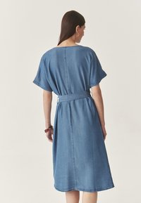 Denim-mekkoinen, jossa on lyhyet hihat, kapea vyötärö ja suora siluetti. Takana on yksinkertainen sauma ja se on polven puoliväliin ulottuva. Vaalea sininen väri.