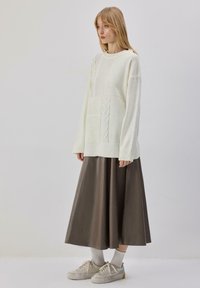 Pull blanc en maille avec motifs texturés, associé à une jupe en cuir marron, et des baskets légères avec des lacets couleur crème et des chaussettes grises.