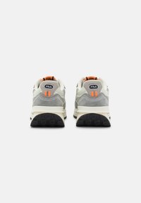 Paire de baskets FILA grises et blanches avec des languettes orange, vues de dos sur un fond blanc.