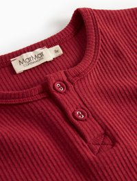 Maglietta rossa a righe con maniche lunghe e scollatura rotonda, con due bottoni frontali e un piccolo dettaglio ricamato. L'etichetta mostra la marca e la taglia (5 anni).