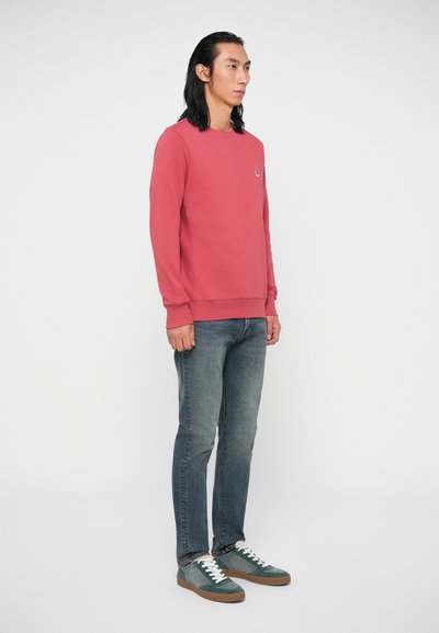 Raudonas megztinis su apvaliu kaklu, pūkuotomis rankovėmis ir šiek tiek elastingas. Dėvimas virš šviesiai mėlynų džinsų ir pilkų sportbačių su baltais raišteliais.