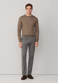 Bruine trui, grijze broek, bruine schoenen. De trui heeft een ronde hals en een aansluitend design. De broek is recht gesneden, van lichtgewicht stof, met een gladde textuur.