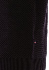 Nahaufnahme eines dunkel strukturierten Strickstoffs mit einem kleinen Union Jack-Tag in der Nähe des gerippten Saums.