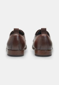 Scarpe in pelle marrone con finitura liscia, silhouette snella, punta arrotondata, tacco basso e dettaglio di linguetta sul retro.