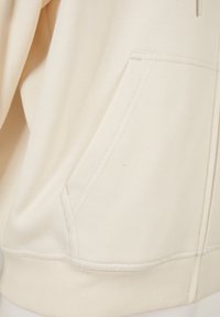 Lichtbeige sweatshirt met een buidelzak, ribgebreide manchetten en zoom, en een zachte, gestructureerde stof met zichtbare stikdetails.