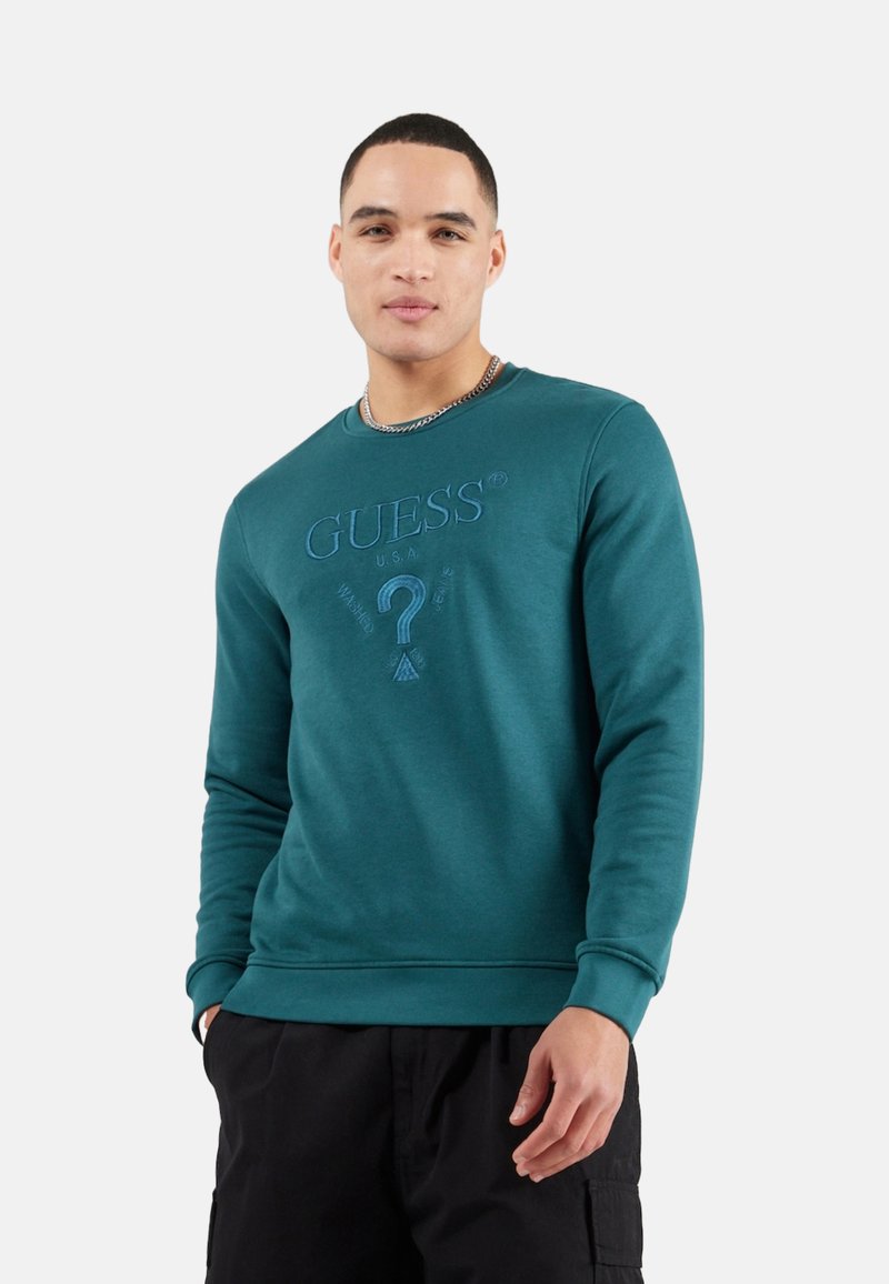 Sudadera teal hecha de una mezcla de algodón, con cuello redondo, mangas largas y un logo bordado con un signo de interrogación en la parte frontal.