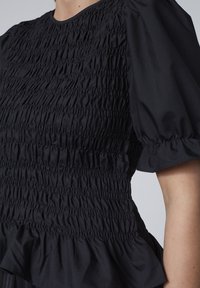 Sort top med smocket tekstur, korte samlet ærmer og peplum kant. Fremstillet af letvægtsstof med en glat overflade.