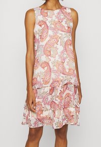 Ærmeløs kjole i lyserød med paisley-mønster i nuancer af rød, orange og guld; har lagdelte flæser i kanten.