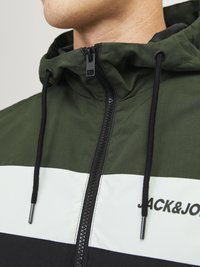 Zeleni jakna s patentnim zatvaračem i kapuljačom; sadrži bijele i crne pruge. Uključuje šnuru i logo sprijeda. Struktuirani materijal.