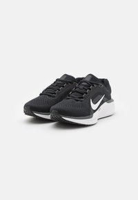 Baskets de course noires avec une tige en mesh, lacets plats, un logo Nike blanc, et une semelle intermédiaire blanche rembourrée. Semelle en caoutchouc texturé pour une meilleure adhérence.