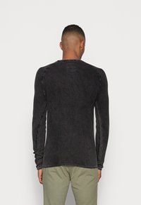 Schwarzes Langarmshirt aus strukturiertem Material, mit Raglanärmeln und kontrastierenden Nähten, kombiniert mit hellen Hosen.