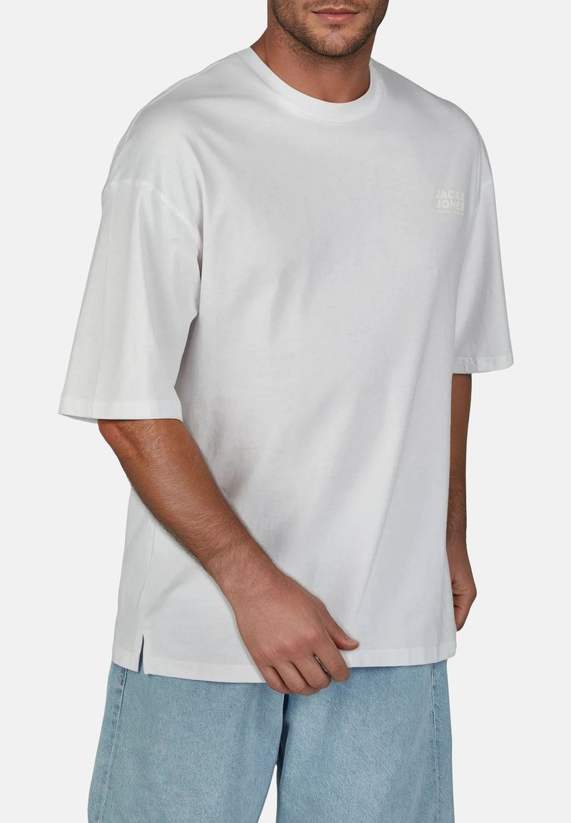 T-shirt bianco a maniche corte in cotone. Presenta un collo a giro e un piccolo logo sul petto. Vestibilità casual con spacchi laterali all'orlo.
