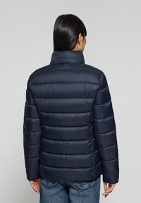 Giubbotto invernale blu navy, con colletto alto, motivo trapuntato orizzontale e finitura lucida e slanciata. Presenta maniche lunghe e una silhouette aderente.