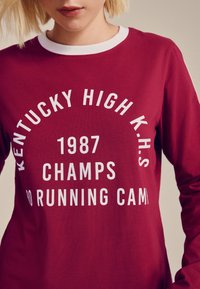 Viininpunainen collegepaita valkoisella pyöreällä kauluksella ja rohkeasti painetulla tekstillä. Teksteissä lukee "KENTUCKY HIGH K.H.S." ja "1987 CHAMPS" eri kokoisina.